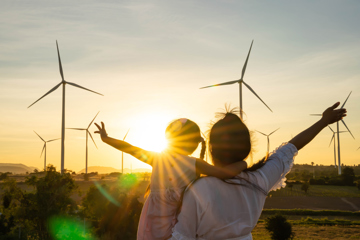 Women And Female Child Cuddling In Front Of Wind Turbines