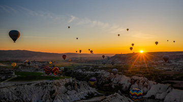 Hot air balloons floating over valleys during sunset
