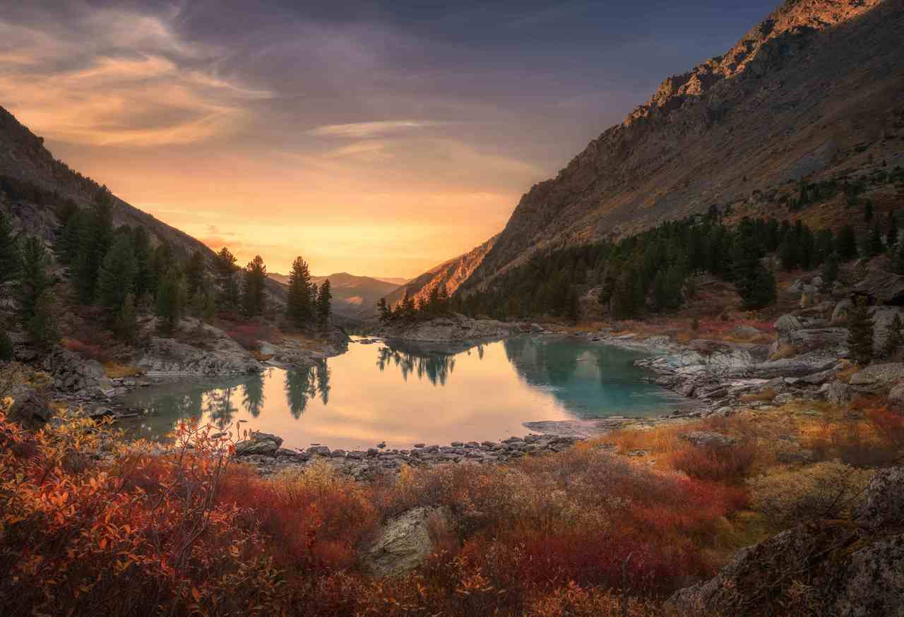 Landscape of a valley in between two mountains with the sun setting, a lake and autumnal foliage