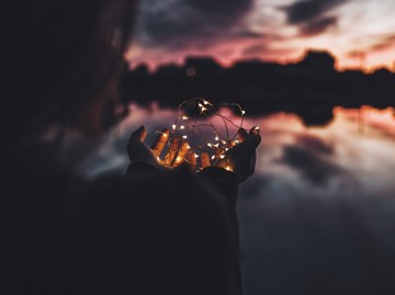Person Holding Fairy Lights Against An Atmospheric Sky